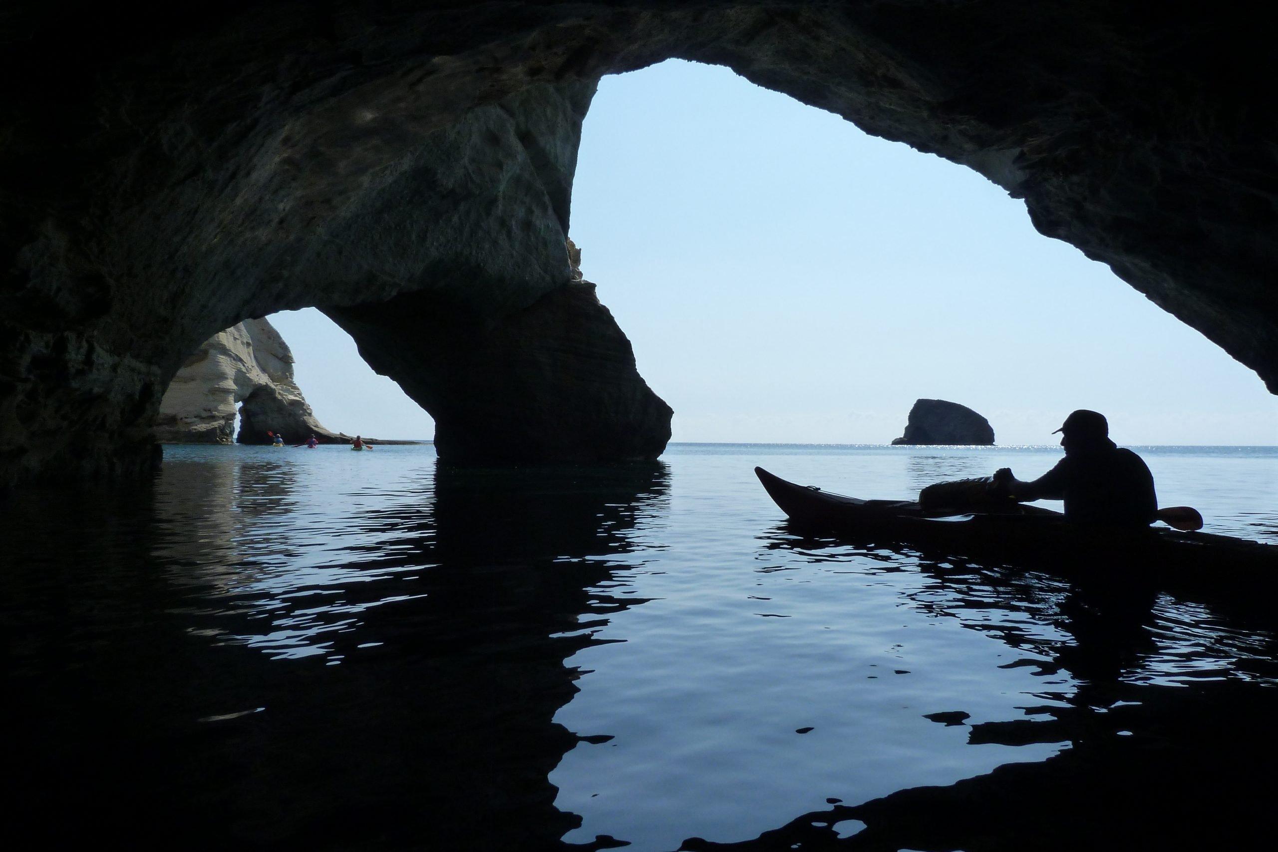 Sea kayak silhouetted inside a Milos arch, looking out to the open Aegean