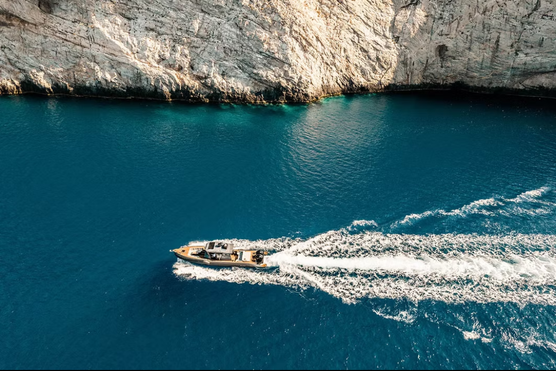 Aerial view of a private boat leaving a wake below the white cliffs of Milos